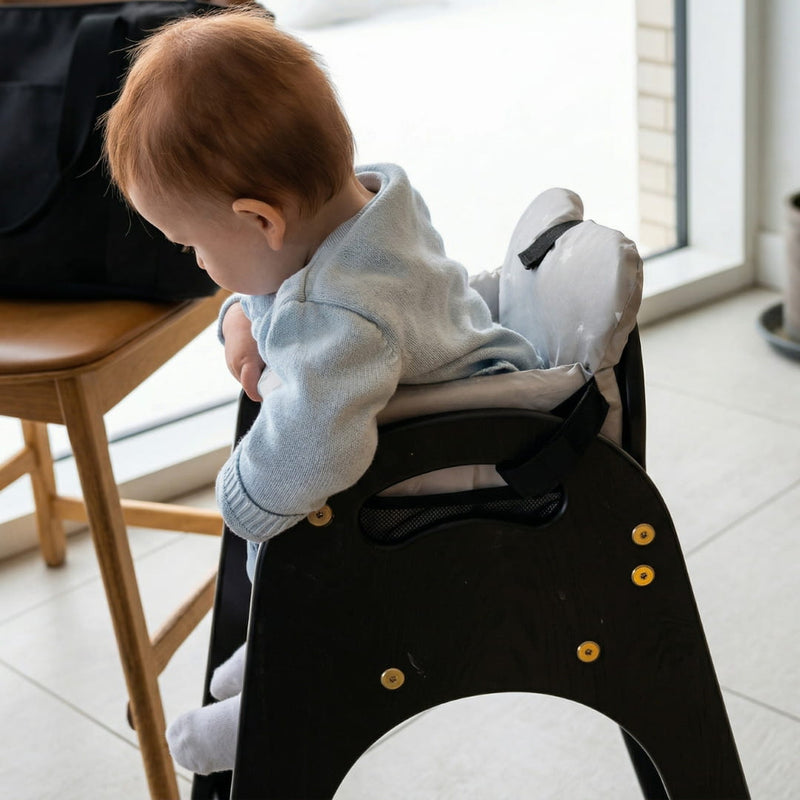 Baby seated in Cocoseat padded insert on black high chair next to dining table