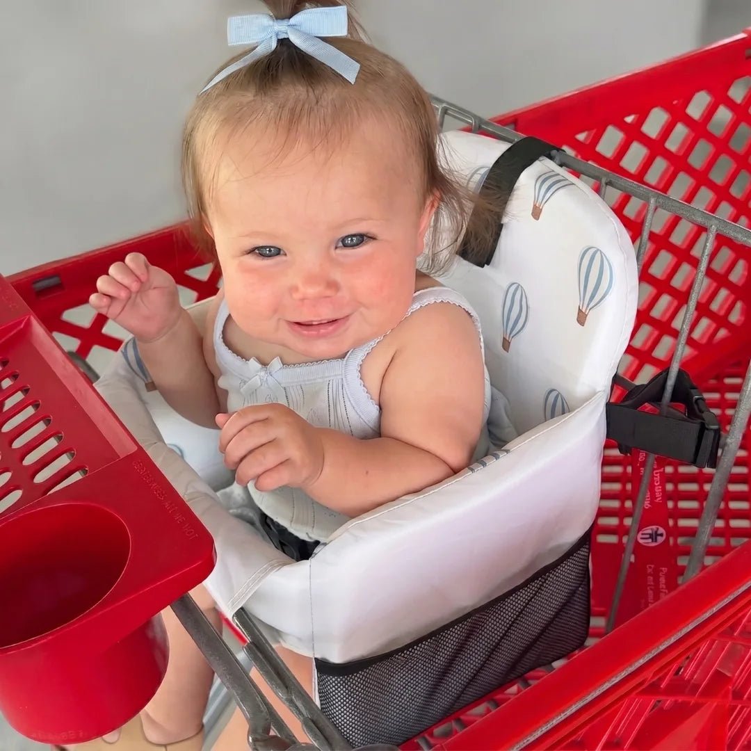 Baby in a high chair inside a red shopping cart with a white background