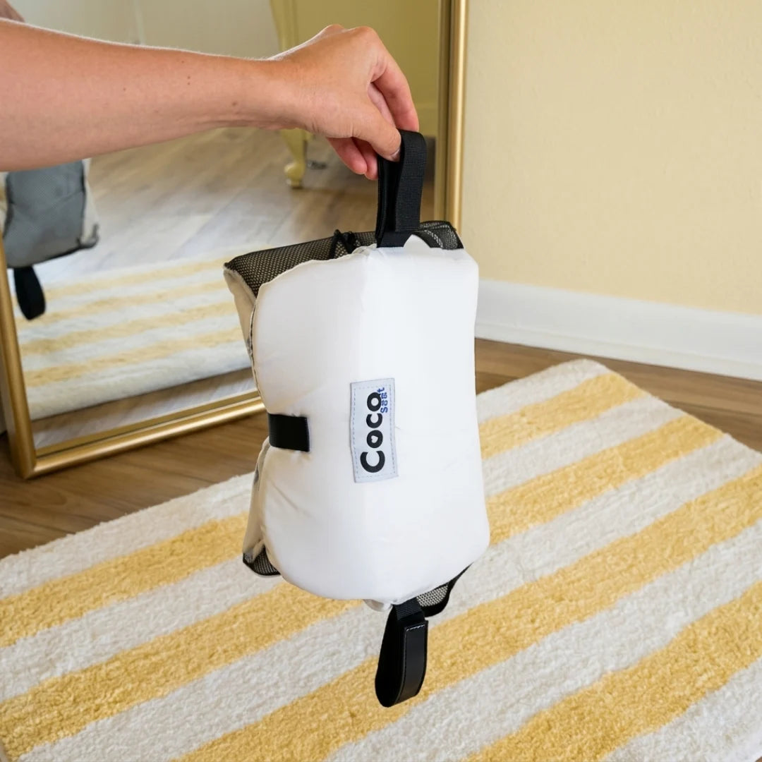 White pet carrier with 'Coco' branding held by a person on a striped rug.