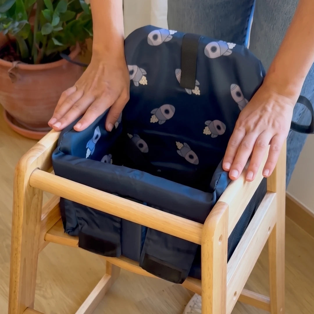 Coco Comfort Seat in navy blue astronaut pattern, hands adjusting the seat inside a wooden high chair