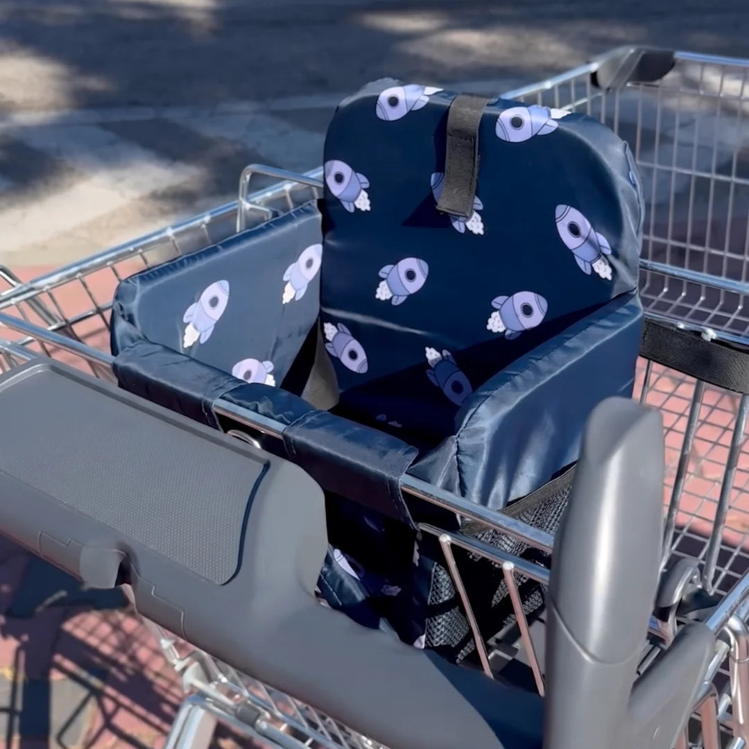 Coco Comfort Seat in navy blue astronaut pattern, installed inside a shopping cart outdoors