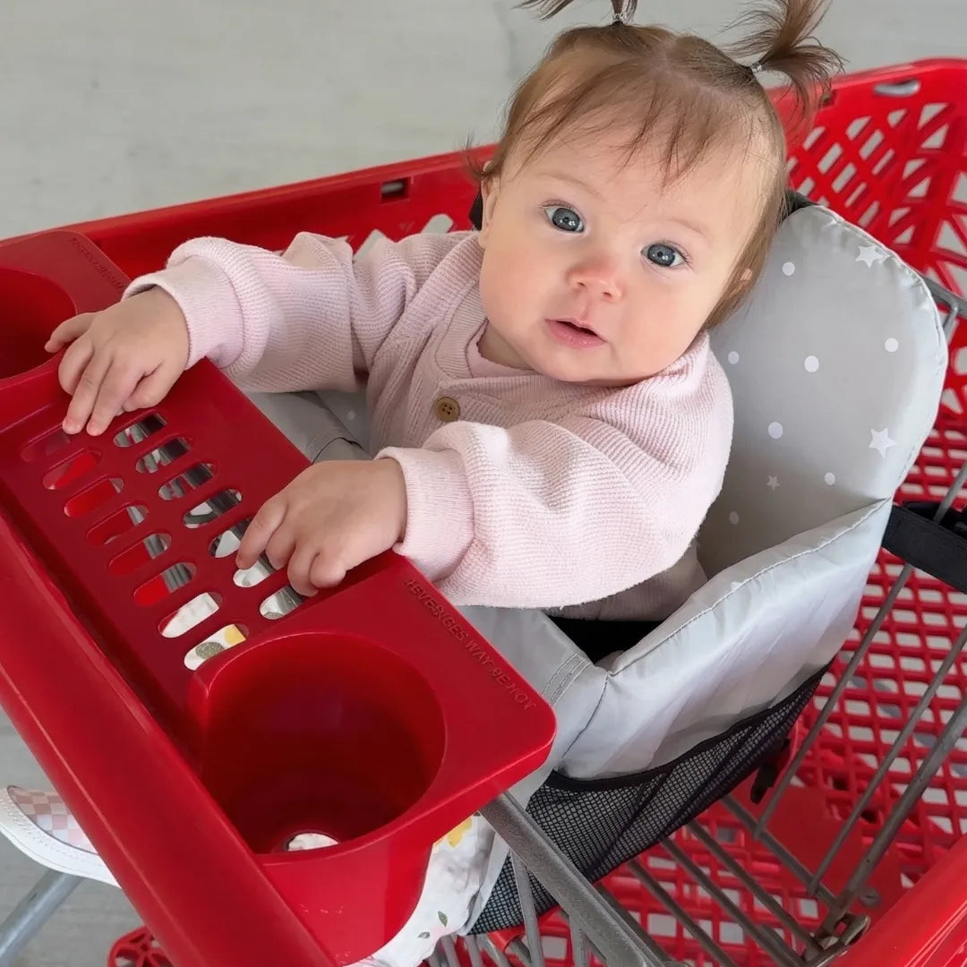 Baby girl sitting safely in Cocoseat padded shopping cart seat insert with star pattern