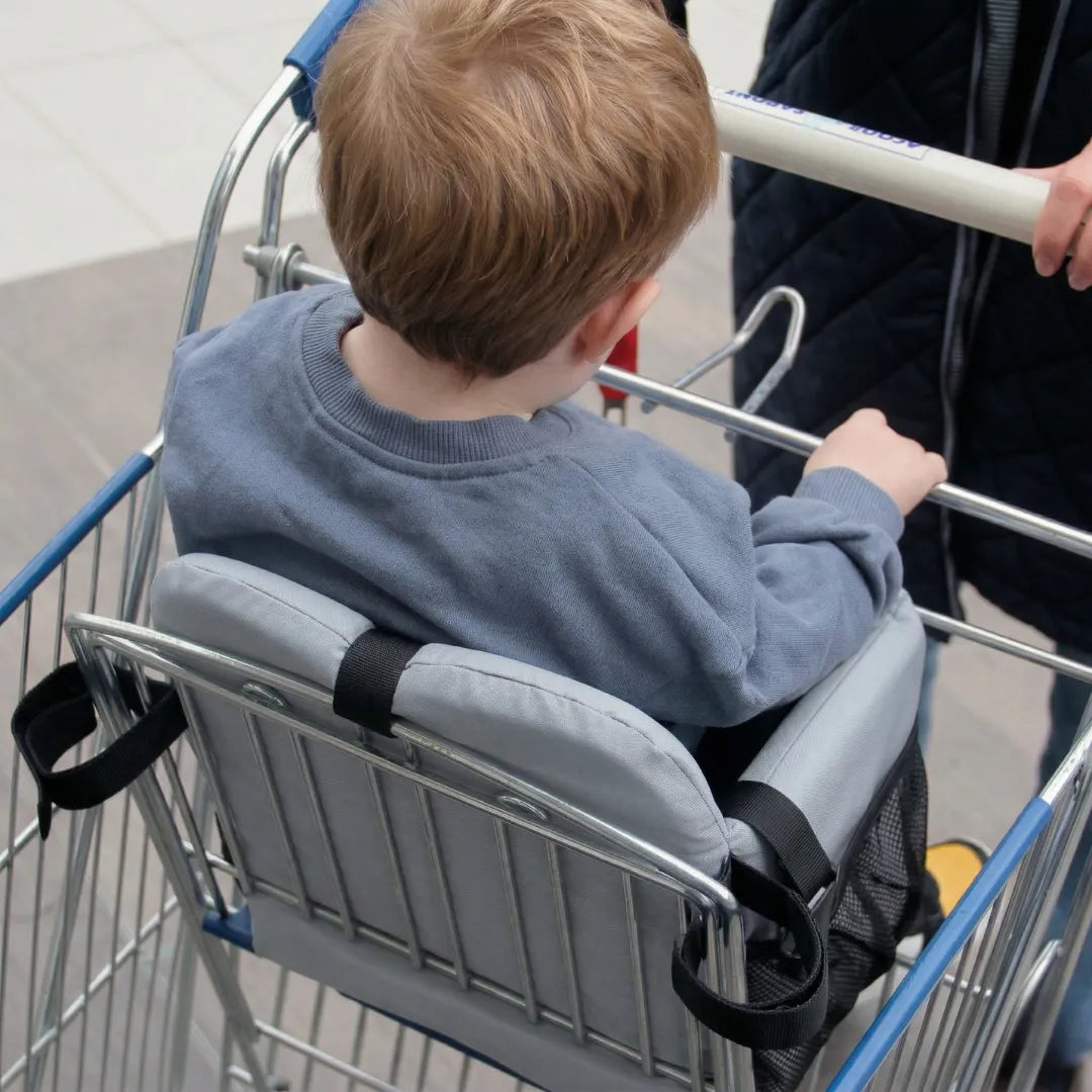 Toddler seated in Cocoseat cart insert, rear view showing securing straps and mesh pocket