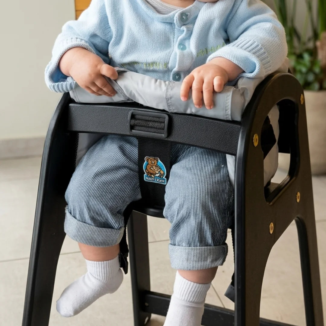 Baby sitting in a Coco Comfort Seat inside a black restaurant high chair