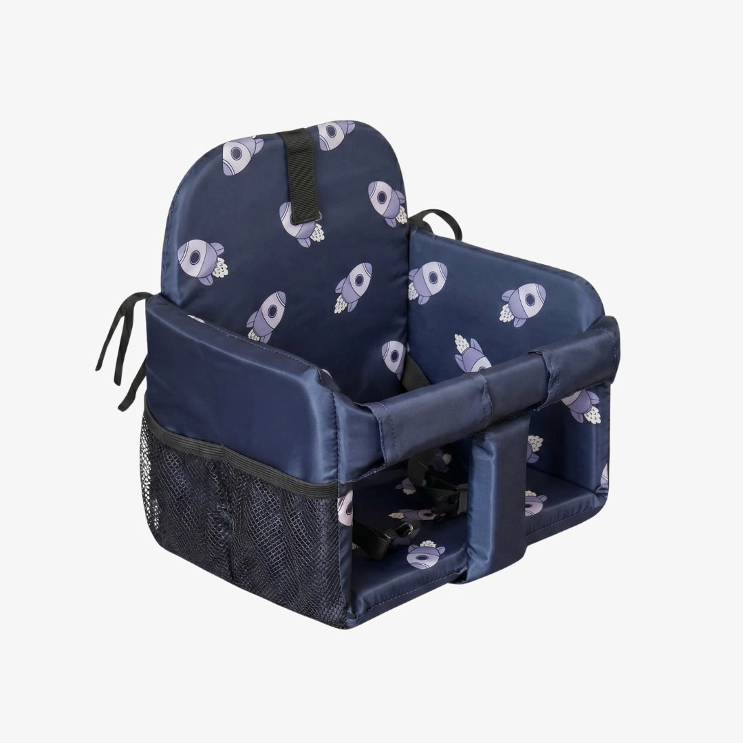 A navy blue child's car seat booster seat with a repeating light purple and white cartoon character pattern on the fabric, featuring a mesh side pocket and black safety harness straps, shown on a light gray background.